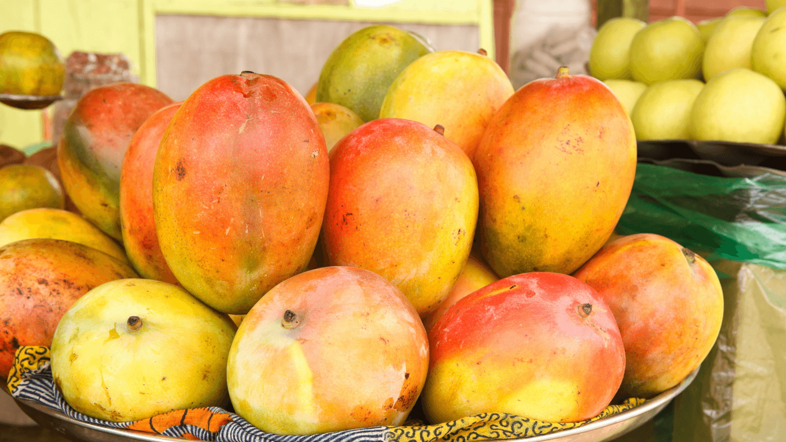A basket filled with ripe African mangoes displayed at a market stall.